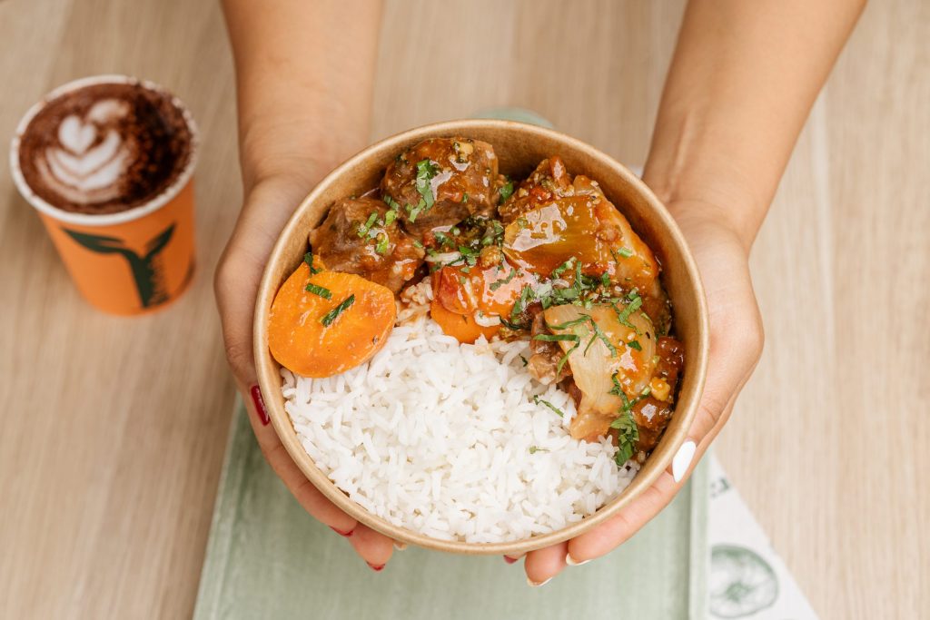 Hand holding a bowl of moroccan beef with rice